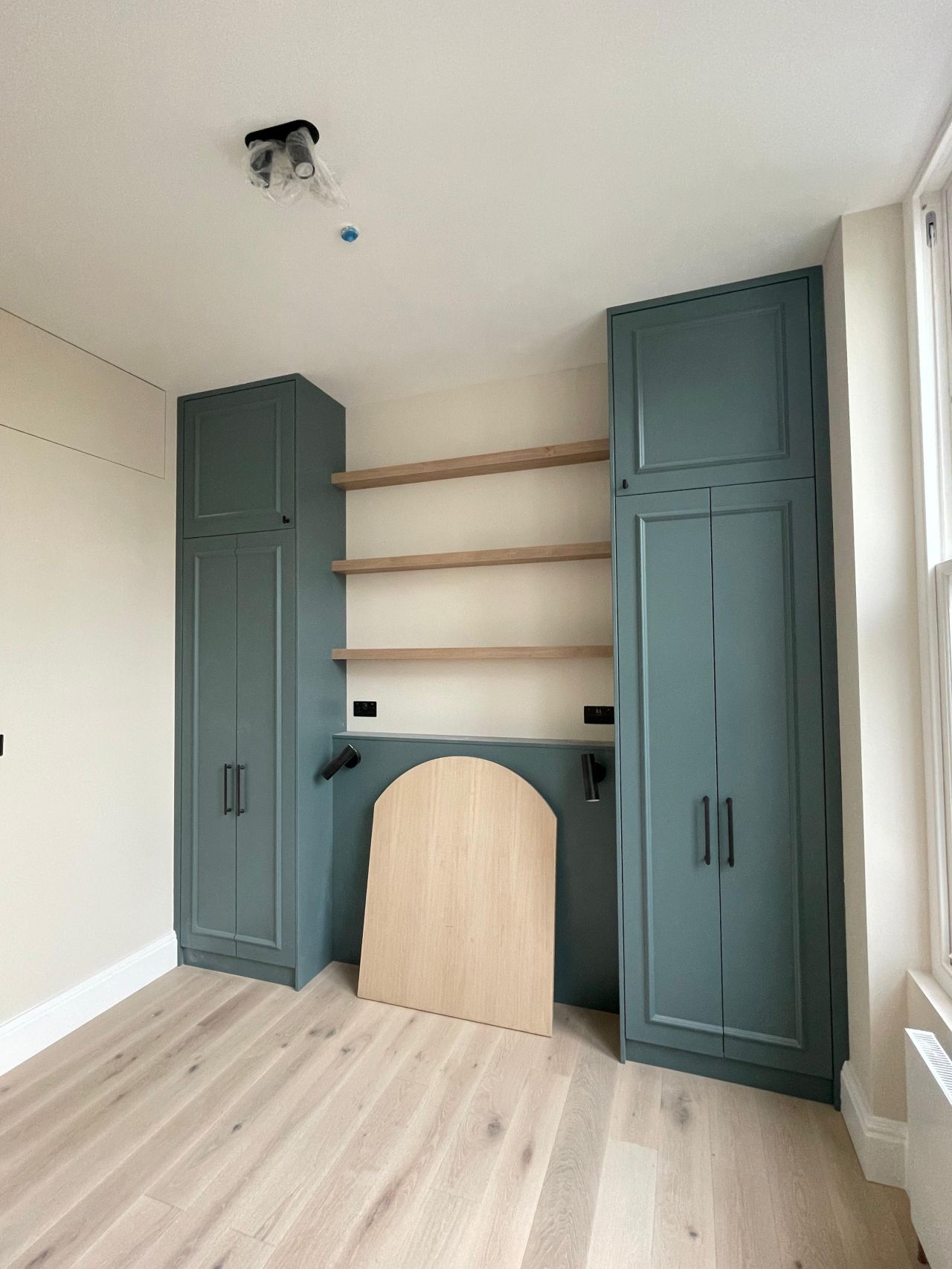Built-in green wardrobes and oak shelving with arched fireplace alcove
